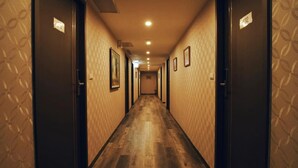 Corredor de hotel com piso de madeira, papel de parede estampado e portas com números de quarto.