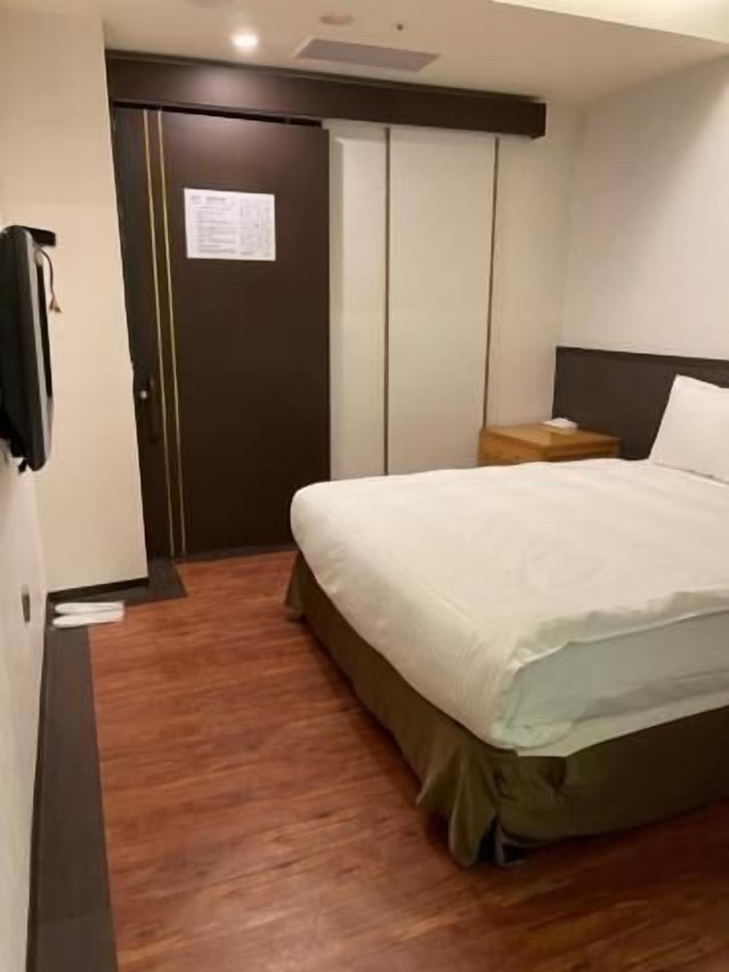Una habitación de hotel con cama, suelo de madera, armario y mesita de noche.