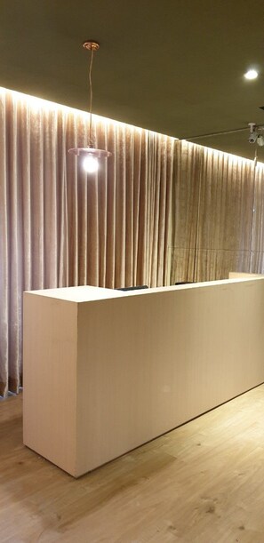 A reception desk with a light fixture above it, a curtain backdrop, and a wooden floor. - Crystal City Hotel (Taoyuan City)