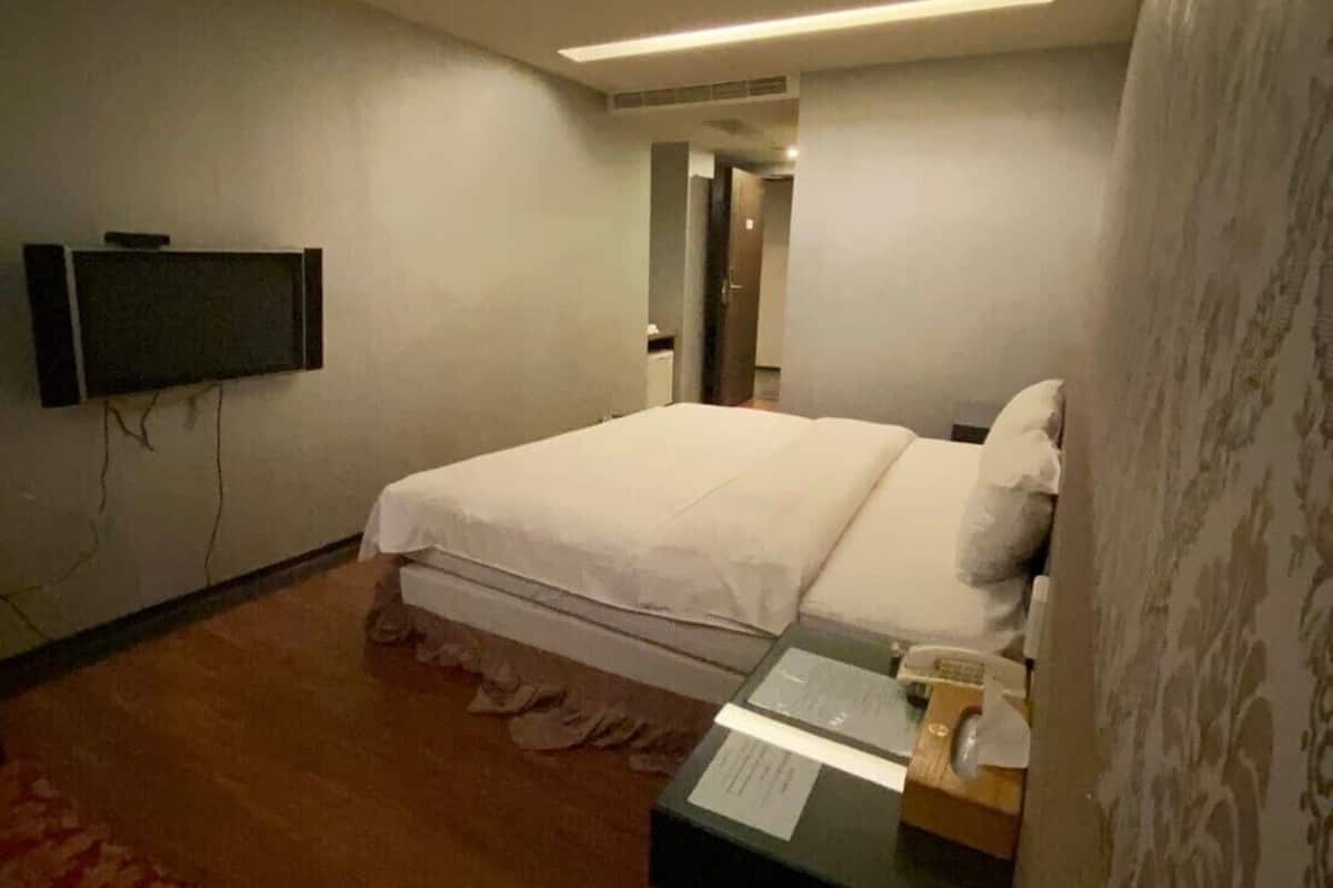 Habitación de hotel con cama, escritorio con teléfono, televisor en la pared y cortina estampada.