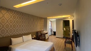 Quarto de hotel com uma cama grande, uma mesa e uma cadeira. Um banheiro é visível ao fundo.