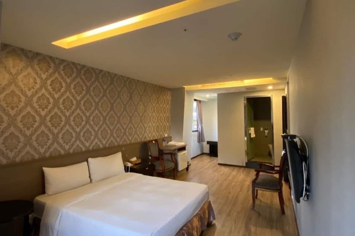 Habitación de hotel con una cama grande, un escritorio y una silla. Se ve un baño al fondo.