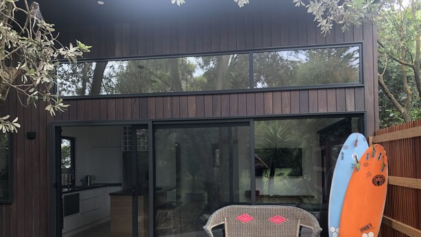 A modern building with a glass door and a wicker bench outside. - The Twisted Mermaid @ Smiths (Smiths Beach)
