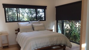 A bedroom with a bed, wooden headboard, bedside tables, and a large window with a view of greenery. - The Twisted Mermaid @ Smiths (Smiths Beach)