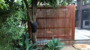 A garden area with a wooden fence, various plants, and a tree with a hanging planter. - The Twisted Mermaid @ Smiths (Smiths Beach)