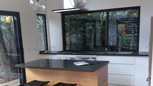 A modern kitchen with a large island, two bar stools, a window with a view of greenery, and pendant lights. - The Twisted Mermaid @ Smiths (Smiths Beach)