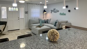 A modern kitchen with a granite countertop, a central island, and a dining area with chairs. - Modern Coastal Home near Siesta Key and Downtown (Sarasota)