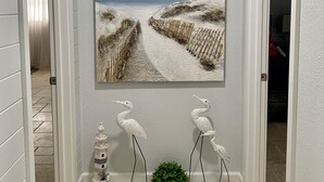 A hallway with a beach painting, two decorative bird sculptures, and a small green plant. - Modern Coastal Home near Siesta Key and Downtown (Sarasota)
