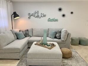 Un salon moderne avec un canapé d’angle gris, un petit pouf et des œuvres d’art décoratives accrochées au mur.