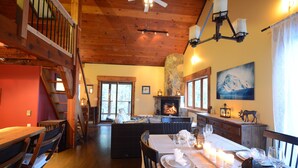 Un comedor acogedor con una mesa de madera dispuesta para dos personas, una chimenea y una escalera que sube a un nivel superior.