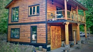 Una cabaña de madera con balcón, rodeada de árboles.