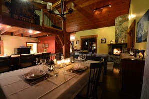 A dining area with a long table set for a meal, a stone fireplace, and a staircase leading to an upper level. - Private Chalet - Relax and unwind or recreate to your heart's content (Mount Currie)