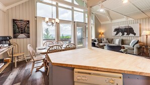 A spacious kitchen with a large island, wooden chairs, and a dining table. There is a sofa and a lamp in the living area. - 1 Mi to Beech Mtn Ski Resort: Home w/ Large Yard (Beech Mountain)