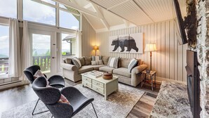 A cozy living room with a sectional sofa, a coffee table, and a fireplace. There is a large window with curtains and a view of the outdoors. - 1 Mi to Beech Mtn Ski Resort: Home w/ Large Yard (Beech Mountain)