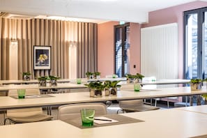 Une salle de conférence avec de longues tables, des chaises, des plantes en pot et des œuvres d’art encadrées accrochées au mur.