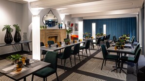 A modern dining area with multiple tables and chairs, a fireplace, and decorative plants. - The Midtown Hotel (Cologne)