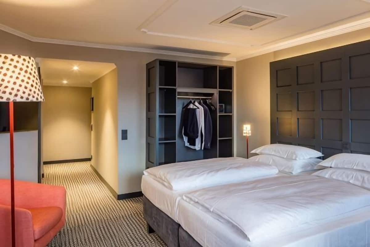 A hotel room with a large bed, a wardrobe, a seating area, and a hallway.