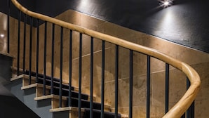 Een wenteltrap met houten leuningen en zwarte metalen spijlen, die uitkomt op een plateau met een lamp.