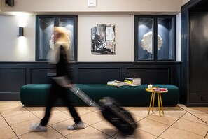 A modern interior with a green sofa, a small yellow table with books, and a wall-mounted artwork. - The Midtown Hotel (Cologne)