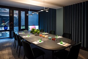 Une salle de conférence moderne, dotée d’une longue table, de chaises noires et d’une grande fenêtre offrant une vue sur les bâtiments environnants.