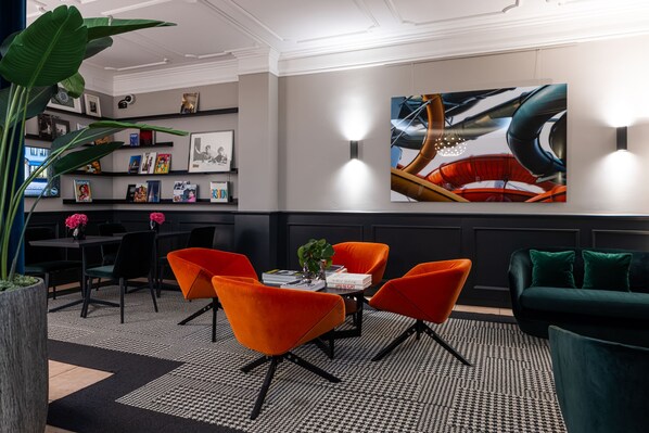 A modern lounge area with a round table, orange chairs, a green sofa, and a large abstract painting on the wall. - The Midtown Hotel (Cologne)