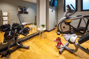 Une salle de sport équipée de matériel d’exercice, d’un tapis de course et d’un miroir qui reflète la pièce.