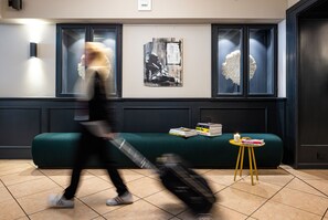 A modern interior with a green sofa, a small yellow table with books, and a wall-mounted artwork. - The Midtown Hotel (Cologne)