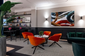 A modern lounge area with a round table, orange chairs, a green sofa, and a large abstract painting on the wall. - The Midtown Hotel (Cologne)
