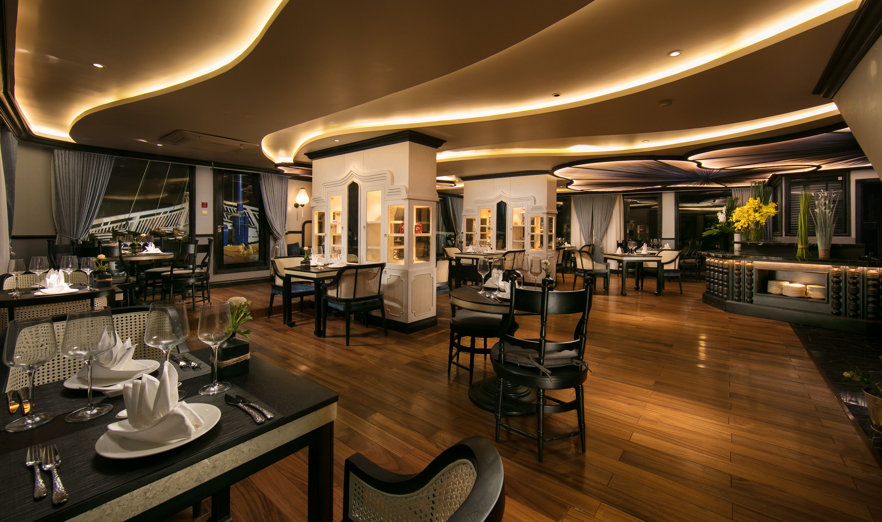 A modern restaurant with wooden flooring, round tables, and black chairs.