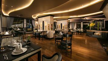 A modern restaurant with wooden flooring, round tables, and black chairs.