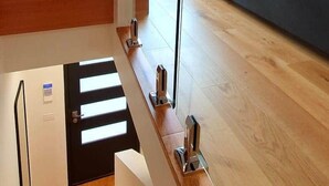Un interior moderno con una escalera de madera, barandilla de vidrio y un sofá gris.