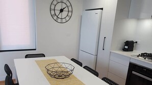 Una cocina moderna con armarios blancos, un refrigerador blanco, una estufa y un reloj en la pared.