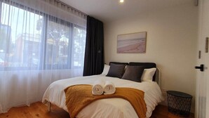 Una habitación de hotel con cama, un cuadro en la pared y una ventana con cortinas.