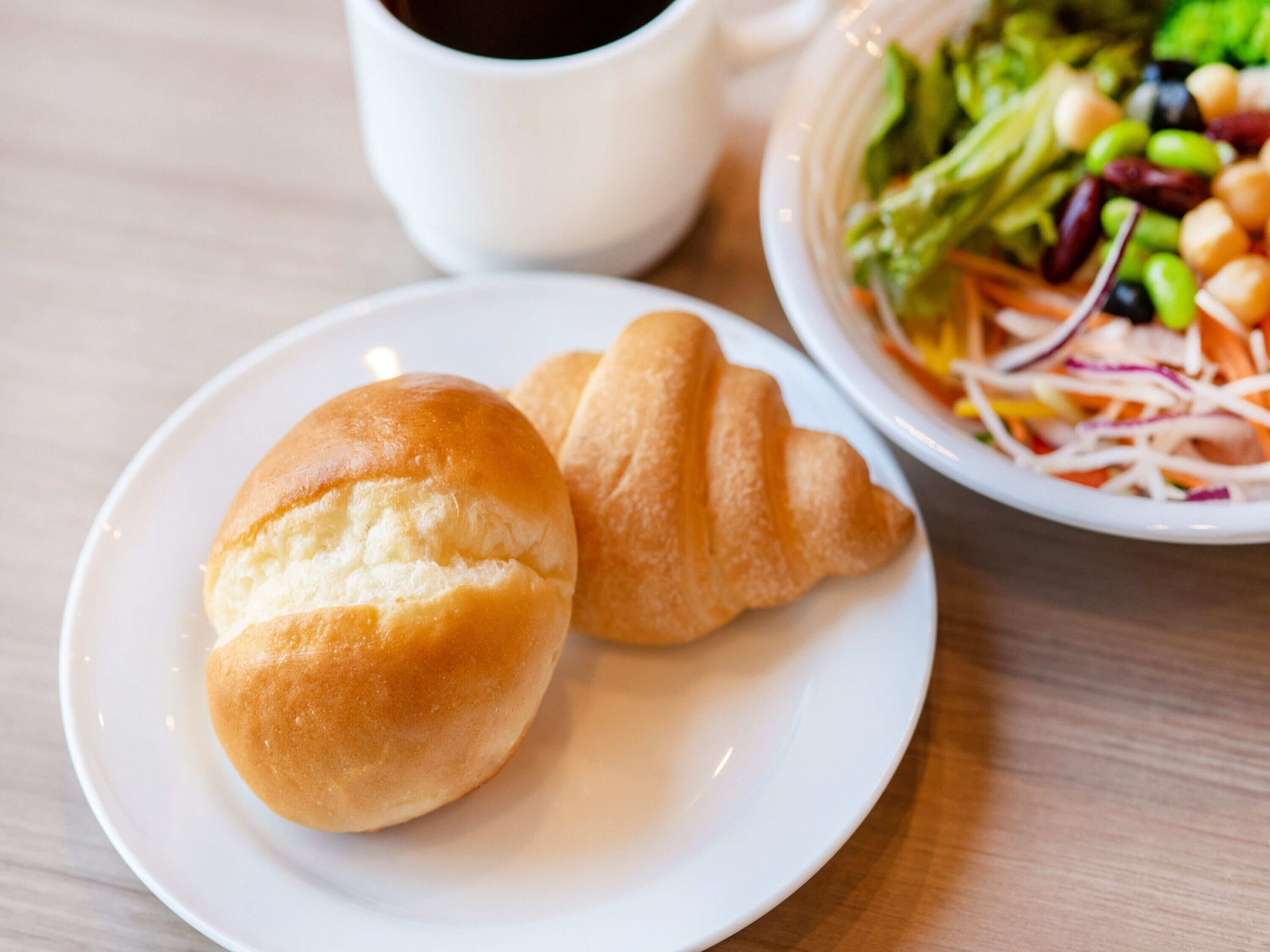 A plate with two croissants and a salad on a table.