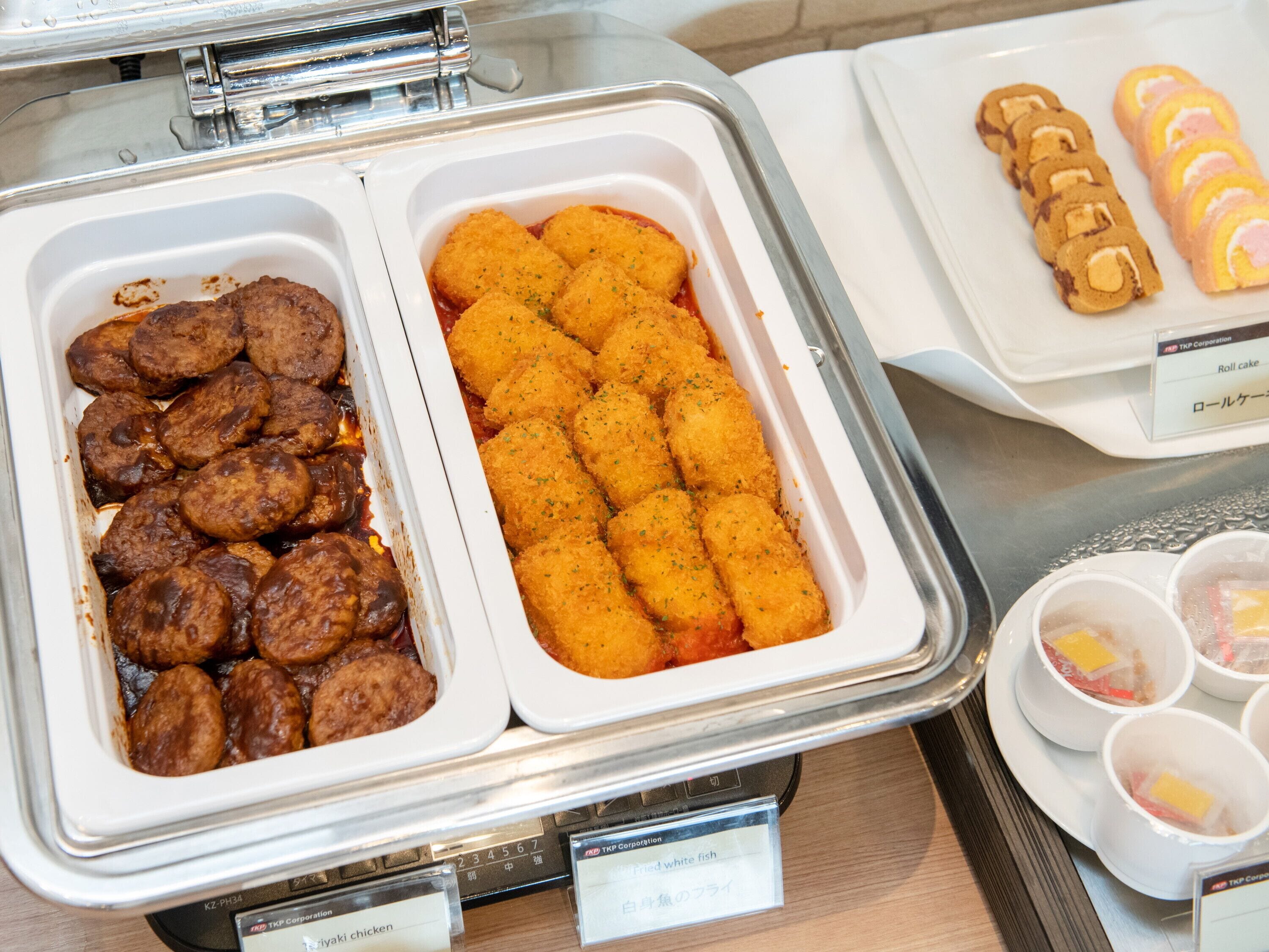 A buffet with various dishes including meatballs, breaded items, and a roll cake.