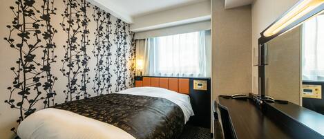 A hotel room with a bed, a desk, a mirror, and a window with curtains.