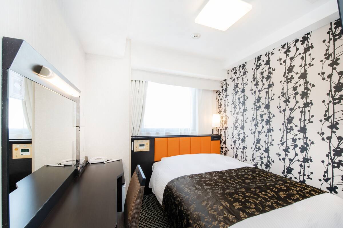 A hotel room with a bed, a desk, a mirror, and a window.