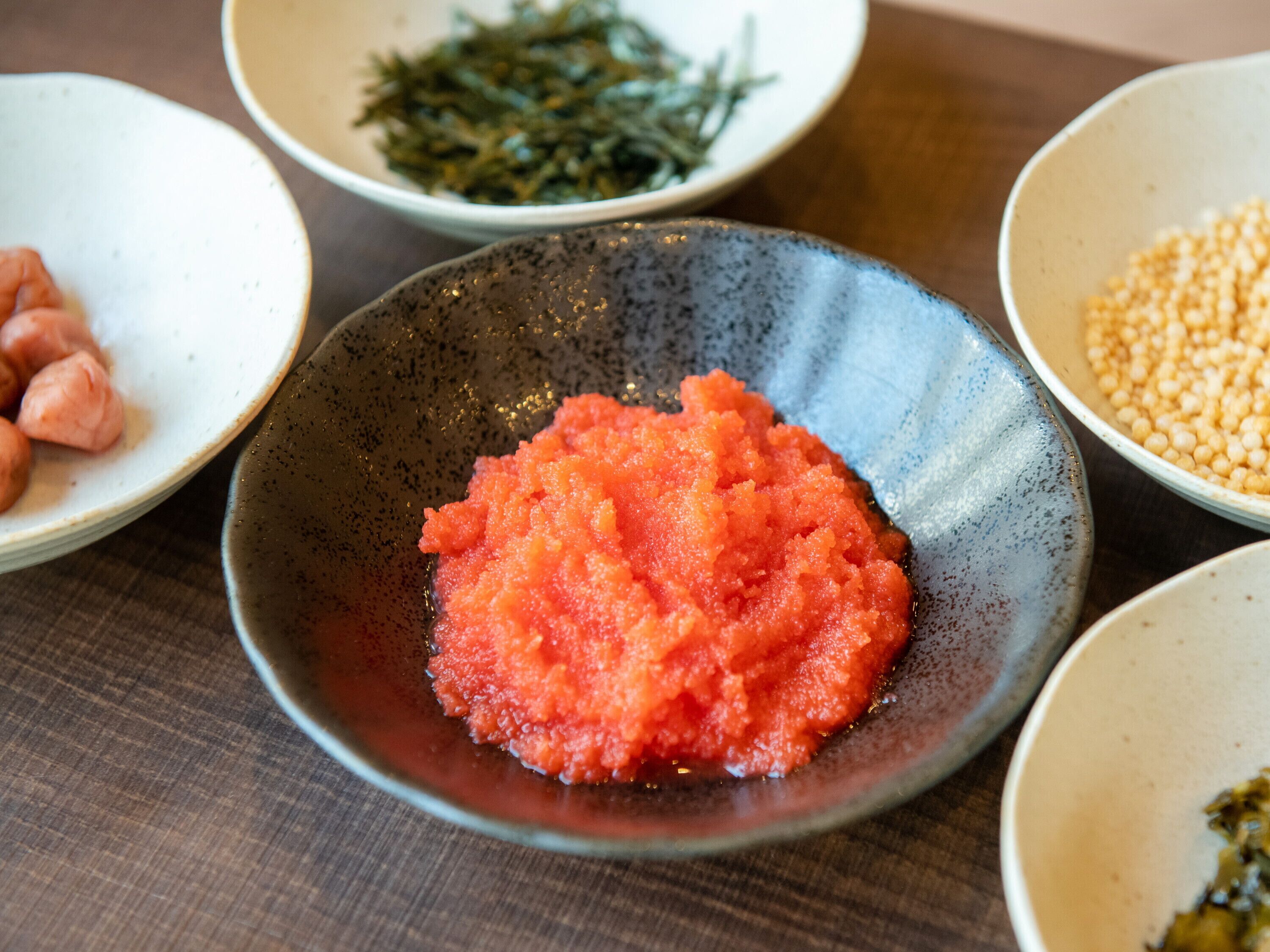 A table with various dishes including a bowl of red food, a bowl of green seaweed, and a bowl of yellow grains.