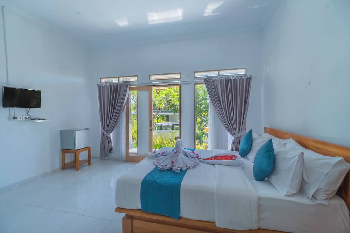 A bedroom with a bed, curtains, a TV, and a view of greenery outside.