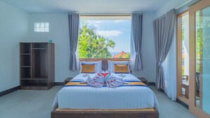 Habitación de hotel con una cama grande, un armario y vistas a zonas verdes y un edificio a través de la ventana.