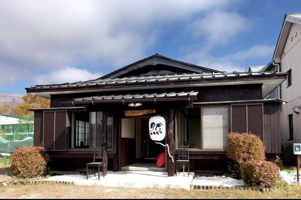 A traditional Japanese house with a dark wooden exterior, a sloped roof, and a sign indicating it is a house. - Guesthouse Zen- Hostel (Yamanakako)