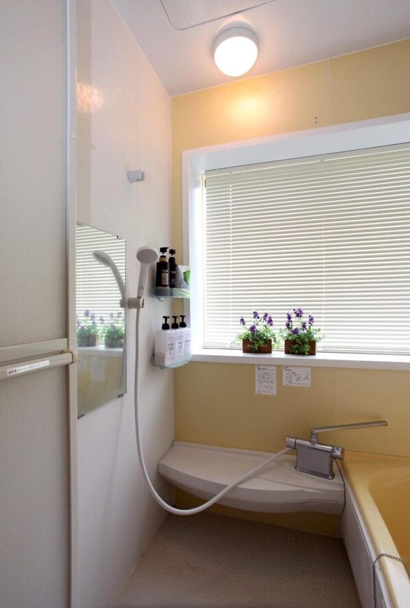 Un baño con ducha, una ventana con persianas y un estante con artículos de aseo.