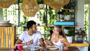 A wooden dining table with two people seated, surrounded by wicker pendant lights and potted plants. - Podpadi Design Spaces (Ubud)