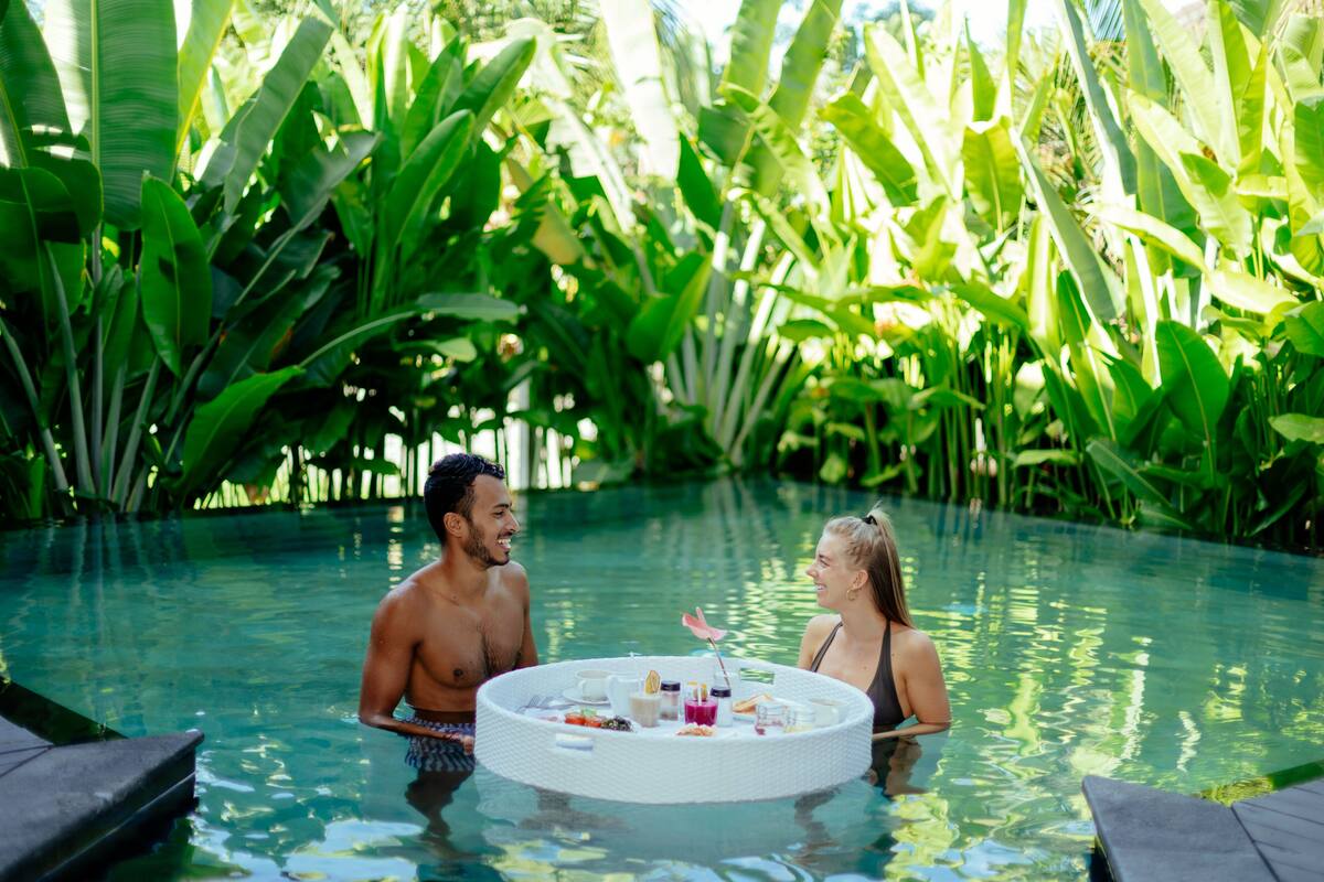 A couple in a circular pool with a table in the center, surrounded by lush greenery.