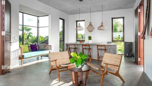 A modern kitchen with a central island, large windows, and a dining area with wicker chairs. - Podpadi Design Spaces (Ubud)