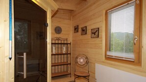 A wooden cabin interior with a glass door leading to a bathroom, a metal shelf with decorative items, a chair, and a window with blinds. - Almhaus Galisch by Interhome (Sirnitz - Hochrindl)