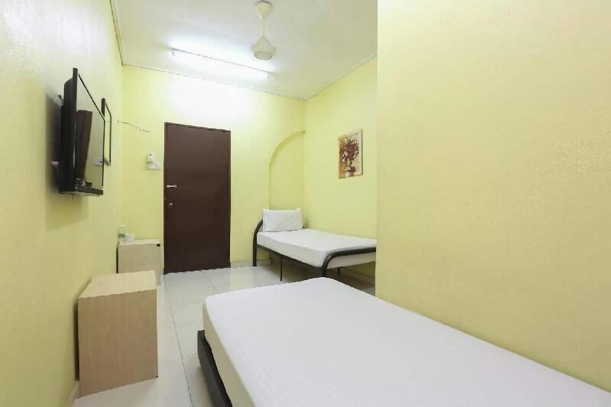 A small, single-bed room with a wooden cabinet, a television mounted on the wall, and a door leading to another room.