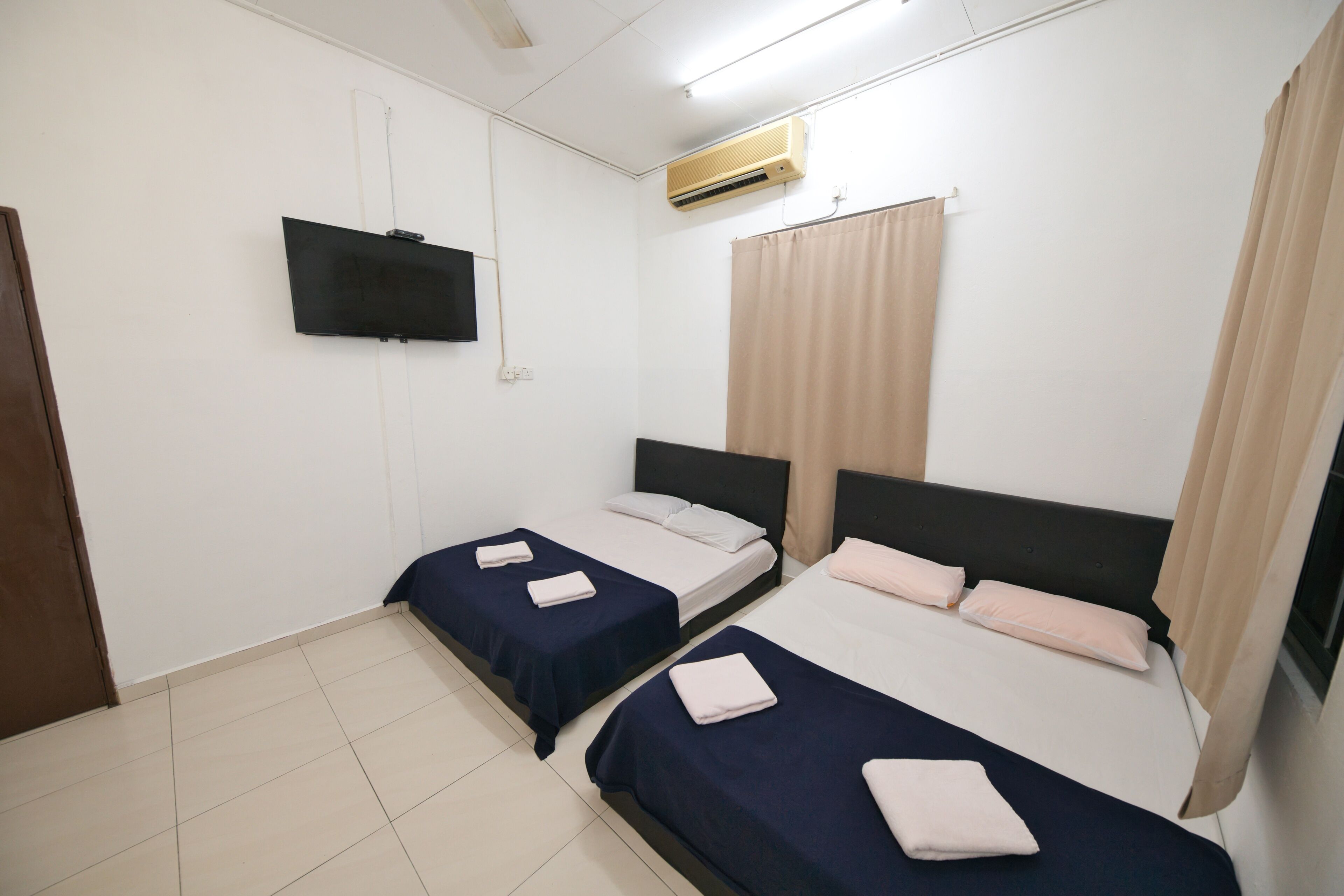 Una habitación con dos camas, un televisor montado en la pared y un aire acondicionado.