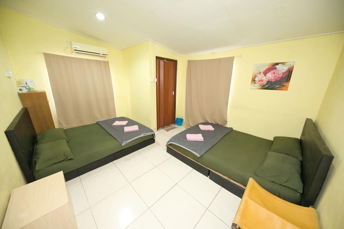 A room with two single beds, a wooden cabinet, an air conditioner, and a door.