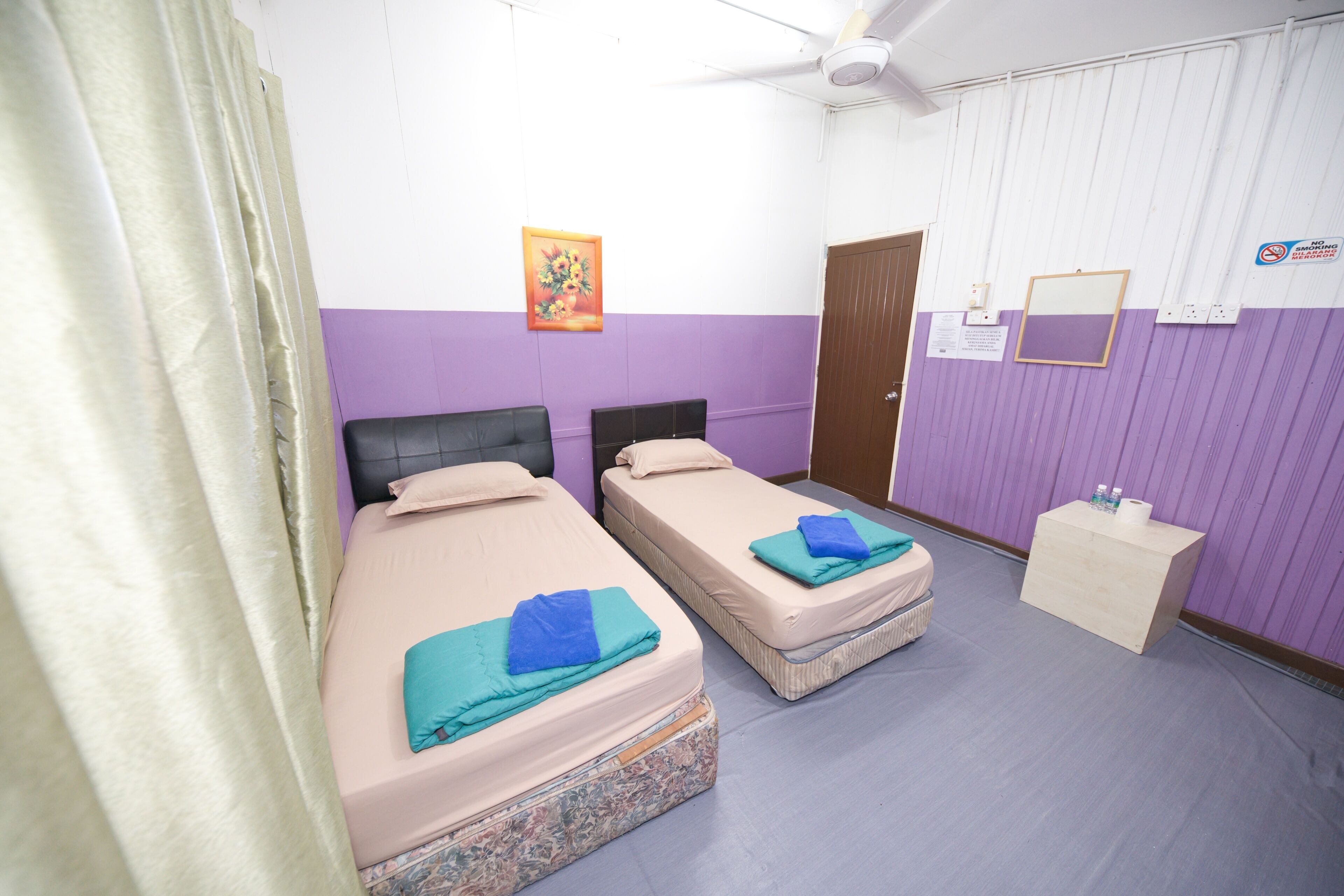 A room with two beds, a wooden nightstand, a ceiling fan, and a door.